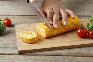 mano femenina cortada en rodajas gyeran mari o tortilla de verduras enrollada coreana con un cuchillo afilado. foto