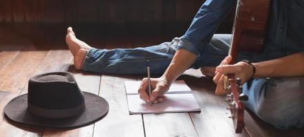 Musicians with acoustic guitars and hipster hats sitting writing songs on paper on a wooden floor at home photo