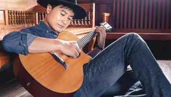 Asian male musician hipster playing acoustic guitar or practicing guitar for leisure or hobby hobby ideas for relaxing holiday at home. photo