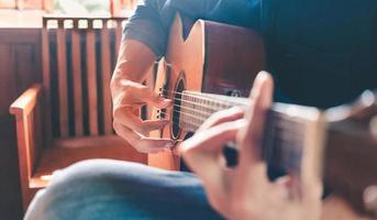 primer plano de las manos y los dedos de un músico masculino tocando una guitarra acústica. instrumento de guitarra musical para recreación o relajación concepto de pasión por el hobby. foto