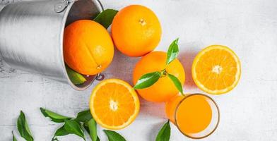 Fresh orange juice and orange fruit are in a basket on a white wooden background.
