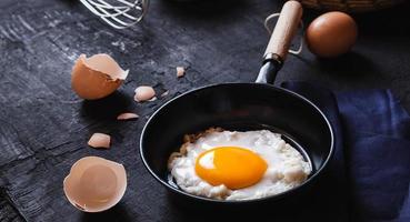 menú de cocina en la cocina huevo frito huevo en la sartén y huevos crudos frescos sobre fondo de madera negra foto