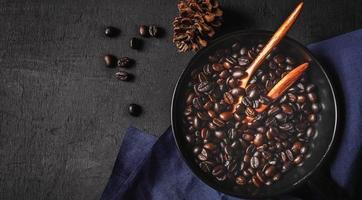 granos de café arábica asados tradicionales y granos de café marrones en una sartén sobre un fondo de madera negra foto