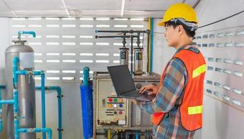 Engineer working in drinking water factory using a tablet computer to check water management system and boiler water pipe in water factory photo