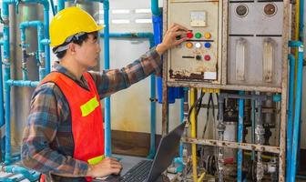 Engineer working in drinking water factory using a tablet computer to check water management system and boiler water pipe in water factory photo