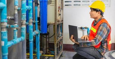 Engineer working in drinking water factory using a tablet computer to check water management system and boiler water pipe in water factory photo