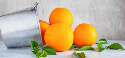 frutas frescas de muchas naranjas en una cesta de acero inoxidable y vierta sobre el fondo blanco de madera. foto
