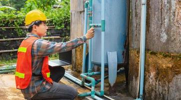 Engineer working in drinking water factory using a laptop computer to check water management system and boiler water pipe  outside the factory photo