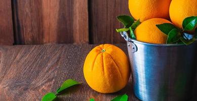 Fresh orange fruit on a wooden table and many oranges in stainless steel basket on wooden background. photo