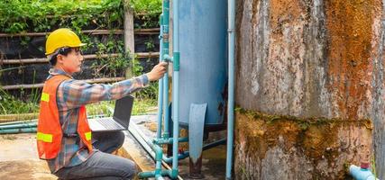 Engineer working in drinking water factory using a laptop computer to check water management system and boiler water pipe  outside the factory photo