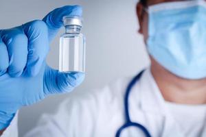 Doctor or researcher Wear blue gloves, work in the laboratory. Pick up a liquid vaccine bottle to treat the coronavirus Or COVID-19. Concept hospital medical services photo