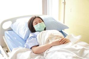 las pacientes asiáticas usan una máscara azul y se acuestan en una cama de hospital. tiene una enfermedad del coronavirus. concepto de servicios médicos, seguro de salud foto