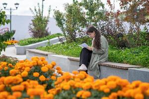 A girl sits on a bench on the street with documents in her hands and using her phone photo