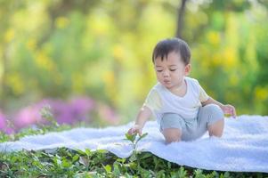 An Asian boy squats on the carpet and uses his hand to pluck a leaf from a tree photo