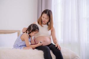 An Asian girl uses a stethoscope to feel her mother's belly to listen to her baby's heartbeat photo