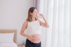 Young Asian woman standing in bedroom drinking a fresh milk, Eat to maintain good health during pregnancy until near childbirth photo