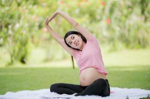 A pregnant Asian woman relaxes with yoga stretching exercises in the park for the health of the mother and the unborn child photo