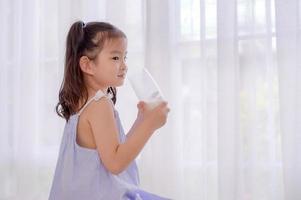 A growing Asian girl sits in her bedroom and enjoys fresh milk for breakfast photo