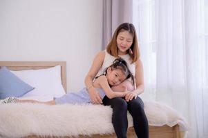 una niña asiática abraza la barriga de su madre para tocar su vientre y escuchar los latidos del corazón de su bebé foto