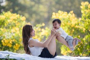 An Asian boy lies on his mother's legs, which are lifted from the cloth floor photo