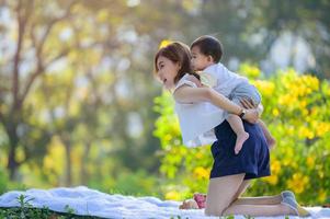 A cute Asian boy perches on his mother's back resting and he enjoys learning outside of school in a nature park photo