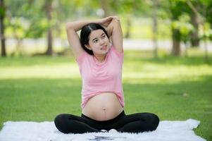 A pregnant Asian woman relaxes with yoga stretching exercises in the park for the health of the mother and the unborn child photo