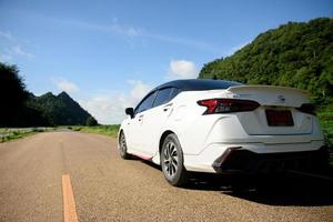 Close-up rear view of a white car with mountains and sky on the road. photo