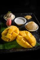 Mango sticky rice, coconut milk, ice cream and macarons on a black plate Popular Thai desserts in summer photo