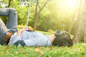 young man resting in the grass with eyes closed listening to music on headphones photo