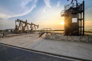 plataforma petrolera o sitio de campo petrolífero, por la mañana o por la noche, las bombas de aceite están funcionando, la bomba de aceite y la hermosa puesta de sol o amanecer de la unidad de bombeo. foto