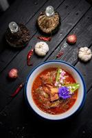 Pork red curry served and decorated with vegetables, herbs and spices on rustic background - Thai food