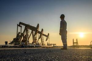 Silhouette of oil workers working in oil rig or oil fields and gas station in the evening with beautiful sunset. photo