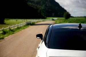 Close-up rear view of a white car with mountains and sky on the road. photo