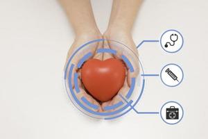 mano que sostiene el corazón rojo con el icono del concepto de atención de la salud, sobre fondo blanco foto