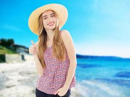 mujer joven elegante muestra como signo en un sombrero de verano de vacaciones en la playa foto