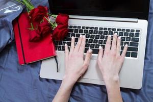 Hands, computer keyboard, bed top view. Workplace background, work at home, notepad and flowers photo