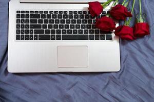 Hands, computer keyboard, bed top view. Workplace background, work at home, notepad and flowers photo