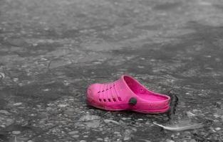 A used and dirty pink plastic shoe, on the shore of a lake. The children's shoe shines in front of a monochrome background. The shore is deserted. photo