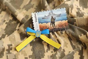 TERNOPIL, UKRAINE - SEPTEMBER 2, 2022 Famous Ukrainian postmark with russian warship and ukrainian soldier as wooden souvenir on army camouflage uniform photo