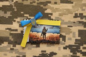 TERNOPIL, UKRAINE - SEPTEMBER 2, 2022 Famous Ukrainian postmark with russian warship and ukrainian soldier as wooden souvenir on army camouflage uniform photo