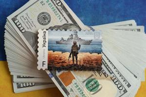 TERNOPIL, UKRAINE - SEPTEMBER 2, 2022 Famous Ukrainian postmark with russian warship and ukrainian soldier as wooden souvenir on big amount of US dollar bills photo