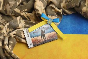 TERNOPIL, UKRAINE - SEPTEMBER 2, 2022 Famous Ukrainian postmark with russian warship and ukrainian soldier as wooden souvenir on army camouflage uniform and national flag photo