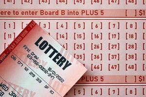 Red lottery ticket lies on pink gambling sheets with numbers for marking to play lottery. Lottery playing concept or gambling addiction. Close up photo