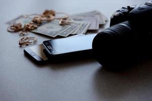 Many expensive golden jewerly rings, earrings and necklaces with big amount of US dollar bills close to smartphones and digital slr camera. Pawn shop photo