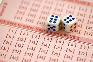 Dice cubes lies on pink gambling sheets with numbers for marking to play lottery. Lottery playing concept or gambling addiction. Close up photo