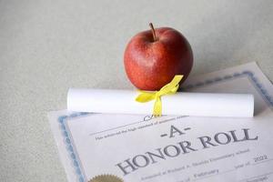 un cuadro de honor se encuentra en la mesa con un pequeño pergamino y una manzana roja. documentos educativos foto