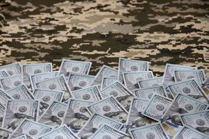 US dollar bills on fabric with texture of Ukrainian military pixeled camouflage. Cloth with camo pattern in grey, brown and green pixel shapes photo