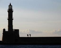 The lighthouse at the port of Chania, Crete, with the silhouette of two backpackers photo