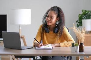 Smiling young African American woman in headphones distracted from computer work look in distance dreaming. Happy biracial female study online at home on laptop thinking or planning. Vision concept. photo