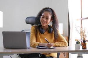 Smiling young African American woman in headphones distracted from computer work look in distance dreaming. Happy biracial female study online at home on laptop thinking or planning. Vision concept. photo